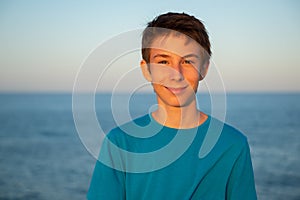 Handsome young happy boy at beach at sunset. Beautiful calm smiling teen boy posing alone at Mediterranean sea coast. Travel,