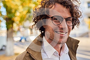 Handsome young happy businessman with glasses smiling and posing outdoors. Male student in autumn street. Smart guy in white shirt