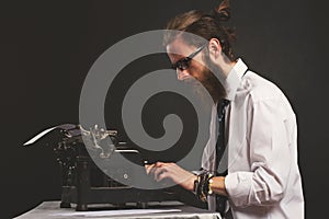 Handsome young hipster businessman thinking and writing with vintage typewriter.