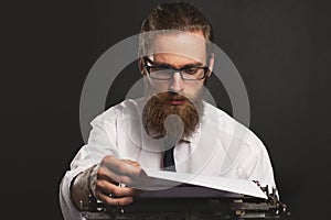 Handsome young hipster businessman thinking and writing with vintage typewriter.