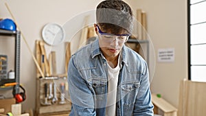 Handsome, young hispanic man standing tall in carpentry work studio â€“ a portrait of dedication and seriousness