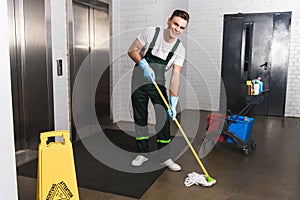 handsome young janitor mopping floor and smiling