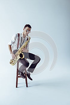 handsome young jazzman sitting on stool and playing saxophone