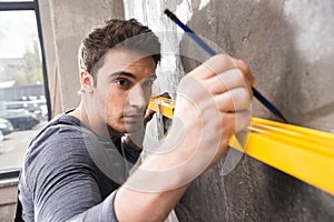 Handsome young laborer with pencil measuring wall with level tool