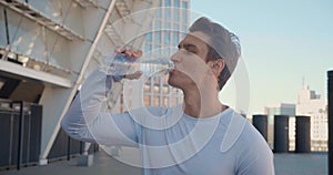 Handsome young male athlete drinking clean water after workout training outdoors on stadium