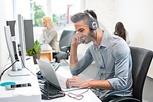 Handsome young male customer service operator working on laptop in office.