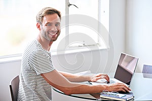 Handsome young male student smiling at camera seated behind laptop