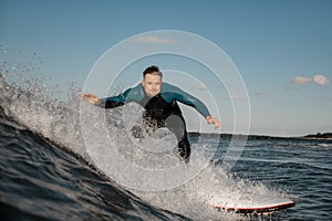 Handsome young male surfer stands in the spray of a wave, riding it on a surfboard