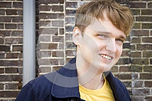 Handsome young man against brick wall smiling.