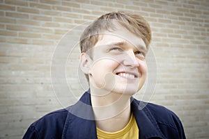 Handsome young man against brick wall smiling.