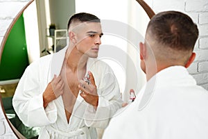 Handsome young man applying perfume in the bathroom