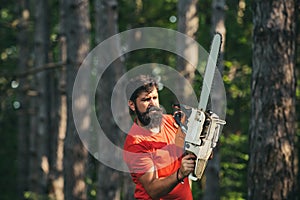 Handsome young man with axe near forest. Logging. Deforestation. Professional lumberjack holding chainsaw in the forest
