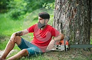 Handsome young man with axe near forest. Lumberjack with chainsaw in his hands. Chainsaw. Deforestation is a major cause