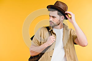 handsome young man with backpack adjusting hat and looking away
