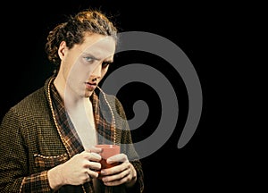 Handsome young man. In a bathrobe with a cup. Man with serious face and brutal style. Copy space. Side view portrait of