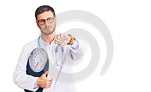 Handsome young man with bear as nutritionist doctor holding weighing machine with angry face, negative sign showing dislike with