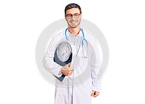 Handsome young man with bear as nutritionist doctor holding weighing machine looking positive and happy standing and smiling with