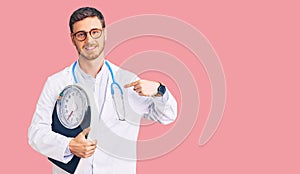 Handsome young man with bear as nutritionist doctor holding weighing machine pointing finger to one self smiling happy and proud