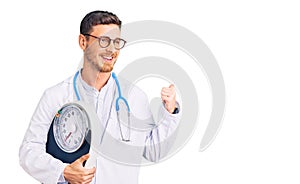 Handsome young man with bear as nutritionist doctor holding weighing machine pointing thumb up to the side smiling happy with open