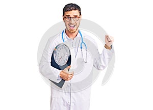 Handsome young man with bear as nutritionist doctor holding weighing machine screaming proud, celebrating victory and success very