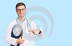 Handsome young man with bear as nutritionist doctor holding weighing machine smiling happy pointing with hand and finger