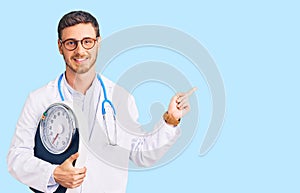 Handsome young man with bear as nutritionist doctor holding weighing machine smiling happy pointing with hand and finger to the