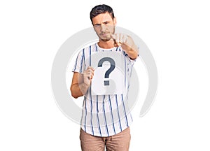 Handsome young man with bear holding question mark pointing with finger to the camera and to you, confident gesture looking