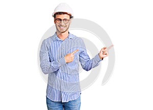 Handsome young man with bear wearing architect hardhat smiling and looking at the camera pointing with two hands and fingers to