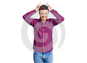 Handsome young man with bear wearing casual shirt posing funny and crazy with fingers on head as bunny ears, smiling cheerful