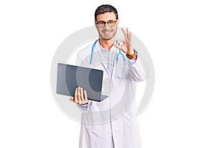 Handsome young man with bear wearing doctor uniform working using computer laptop doing ok sign with fingers, smiling friendly