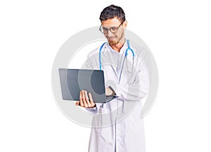 Handsome young man with bear wearing doctor uniform working using computer laptop looking positive and happy standing and smiling