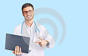 Handsome young man with bear wearing doctor uniform working using computer laptop smiling happy pointing with hand and finger