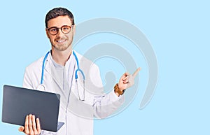 Handsome young man with bear wearing doctor uniform working using computer laptop smiling happy pointing with hand and finger to