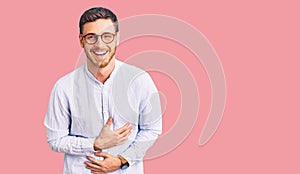 Handsome young man with bear wearing elegant business shirt and glasses smiling and laughing hard out loud because funny crazy