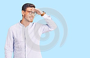 Handsome young man with bear wearing elegant business shirt and glasses very happy and smiling looking far away with hand over