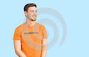 Handsome young man with bear wearing tshirt with happiness word message looking away to side with smile on face, natural