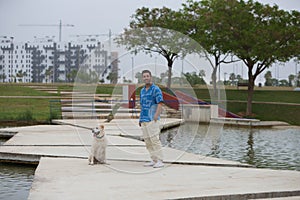 Handsome young man with beard and his Labrador retriever dog, posing for photos by a lake in the park. The man shows his affection