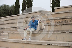 Handsome young man with beard and his Labrador retriever dog stop to rest on a grandstand. Concept pets and companion animals.