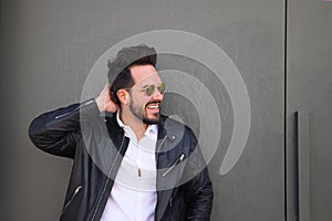 Handsome young man with beard, sculpted body and sunglasses stands at the grey door of his garage while doing different poses for