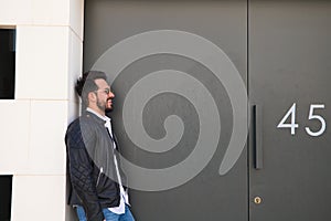 Handsome young man with beard, sculpted body and sunglasses stands at the grey door of his garage while doing different poses for