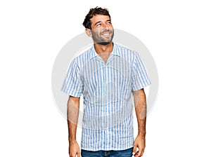 Handsome young man with beard wearing casual fresh shirt looking away to side with smile on face, natural expression