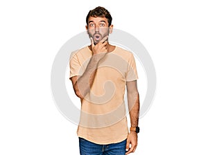 Handsome young man with beard wearing casual tshirt looking fascinated with disbelief, surprise and amazed expression with hands