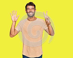 Handsome young man with beard wearing casual tshirt showing and pointing up with fingers number seven while smiling confident and