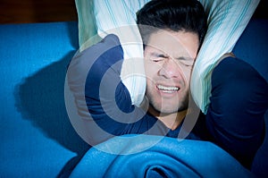 Handsome young man in bed suffering insomnia and sleep disorder, covering his ears with a pillow, above view