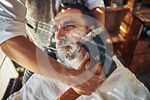 Handsome young man being shaved with an axe