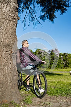 Handsome young man with bicycle in the park on a sunny day