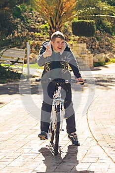 Handsome young man with bicycle showing thumbs up in park on sunny day