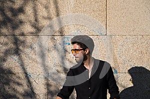 Handsome young man with black shirt and yellow sunglasses on brown background making different expressions and smiling