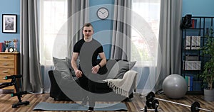 Handsome Young Man in a Black T-Shirt and black gym suit doing stretching at home. Handsome Guy doing warm up in Living Room at