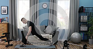 Handsome Young Man in a Black T-Shirt and black gym suit doing stretching at home. Handsome Guy doing warm up in Living Room at
